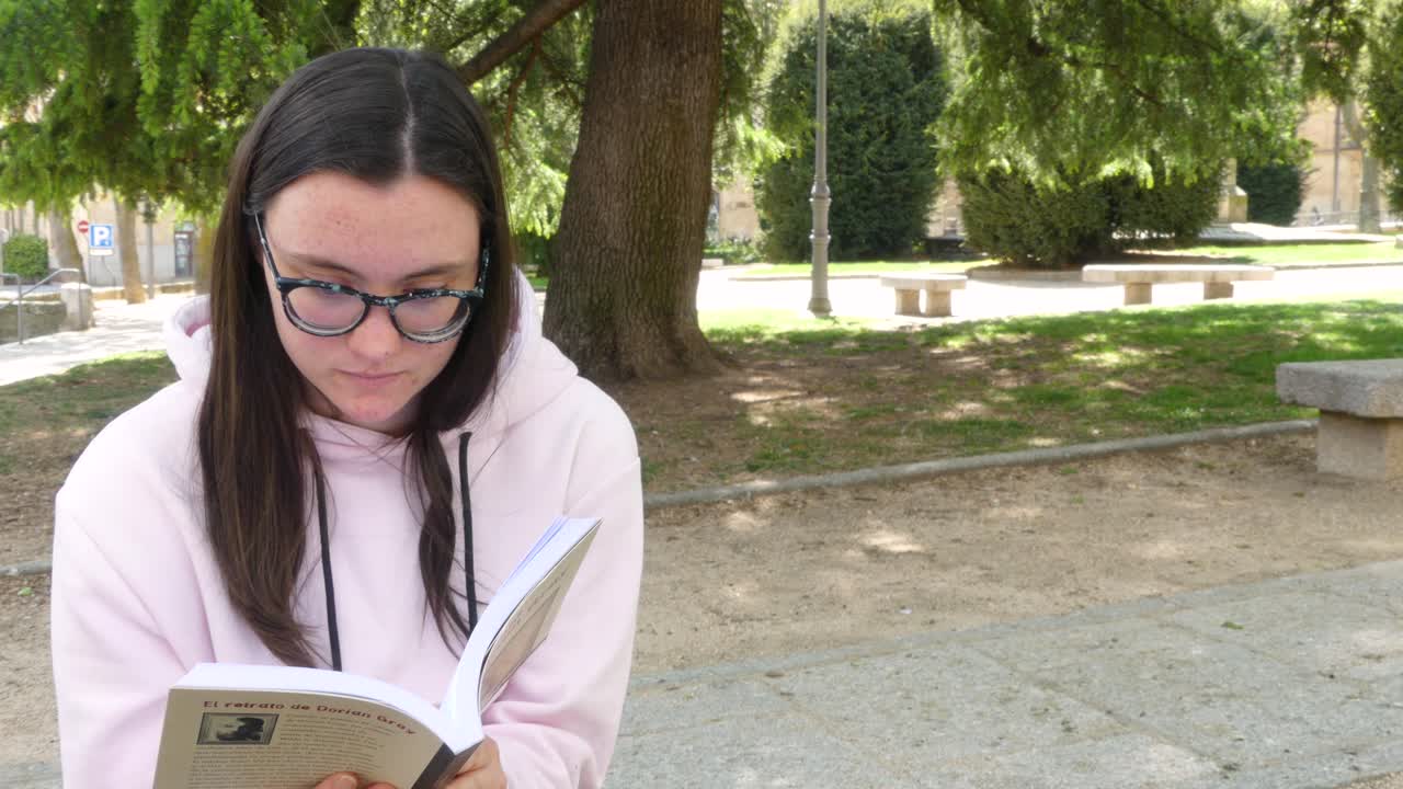 linda chica leyendo una novela en la calle, al lado de un parque