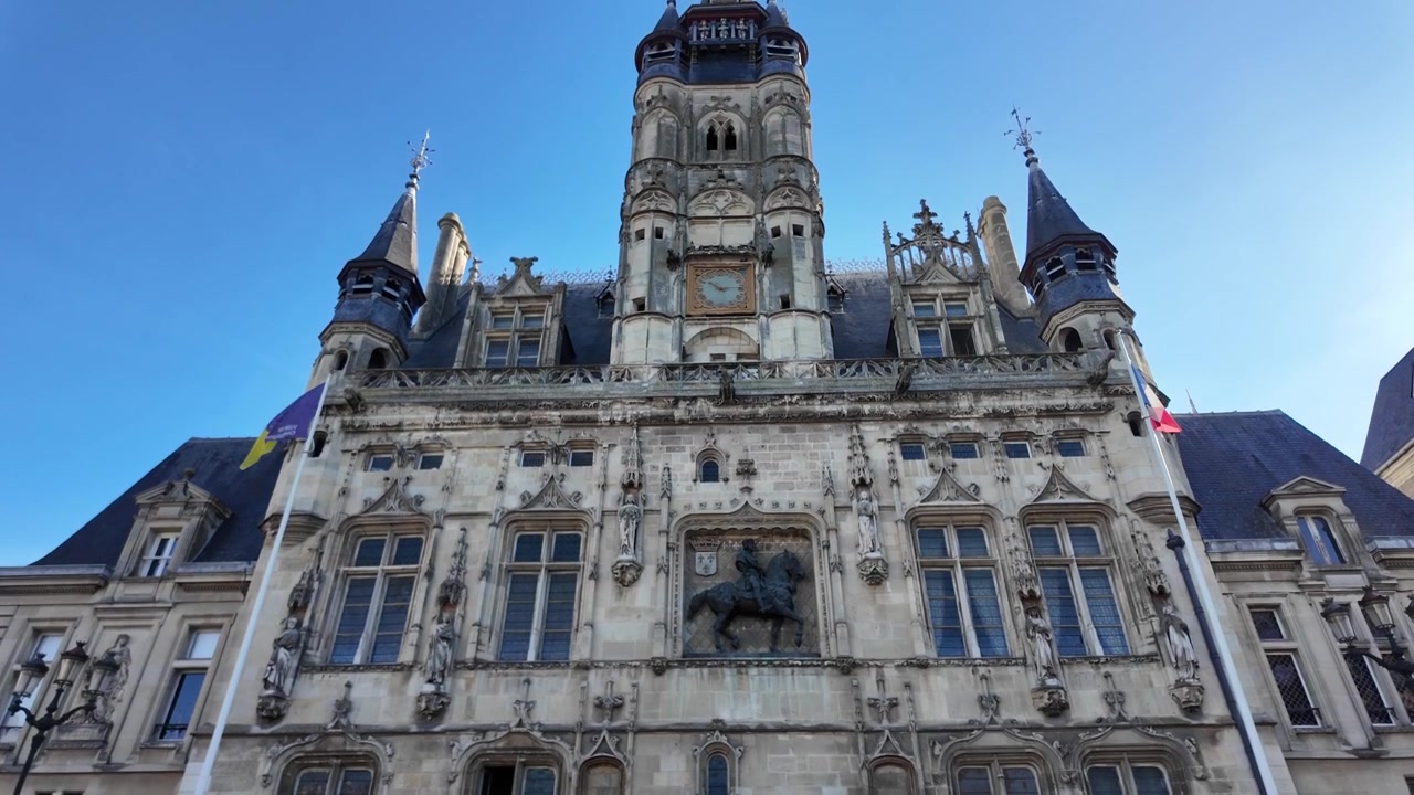 Vista frontale del Municipio di Compiègne caratterizzato da decorazioni in pietra, finestre gotiche, statue, torrette, una torre centrale e una scultura equestre