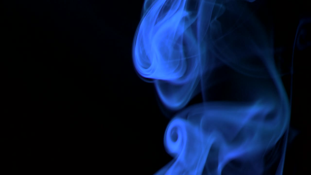 Fumo blu neon che sale lentamente in eleganti volute verso l'alto. Fumo colorato che si diffonde dal basso verso l'alto. Primo piano, isolato su sfondo nero.