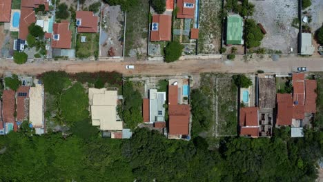 Aerial-drone-birds-eye-top-view-shot-of-a-white-car-driving-down-a-dirt-road-in-the-rural-residential-area-of-the-tropical-beach-town-of-Tibau-do-Sul-in-Rio-Grande-do-Norte,-Brazil