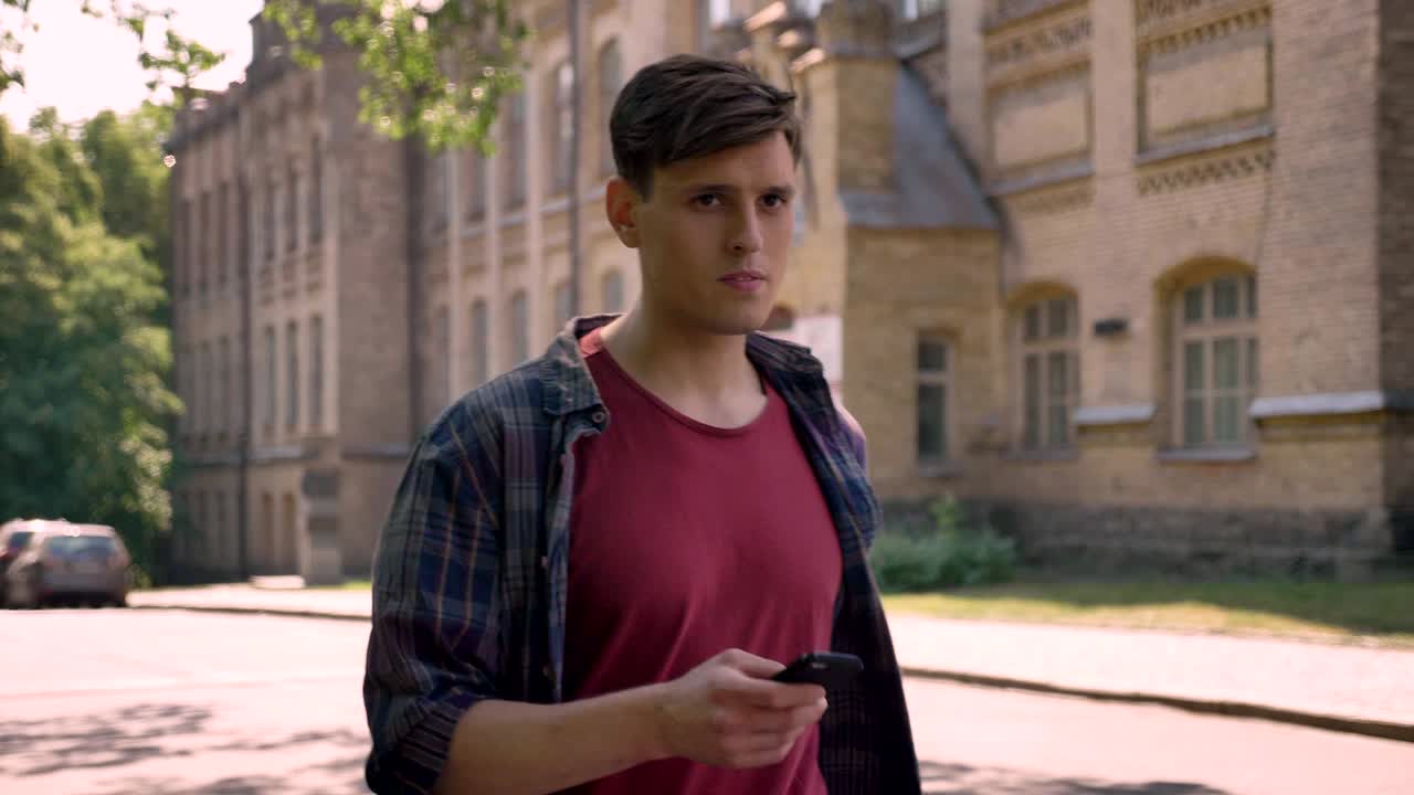 молодой симпатичный мужчина идет по улице в дневное время летом, нажимая на смартфон, звонок, концепция связи