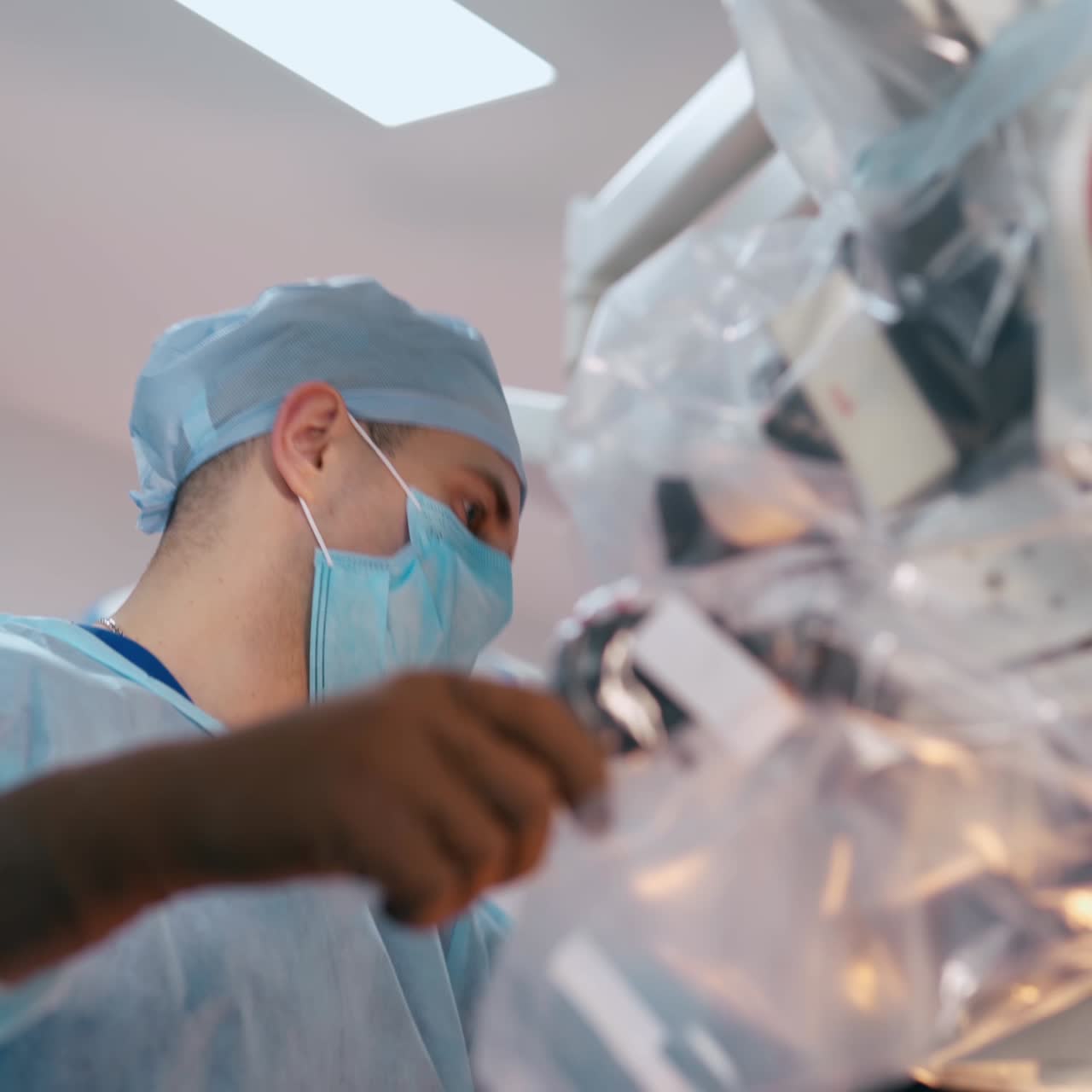 Surgeon uses modern medical equipment. Male specialist in medical uniform looking into the microscope in the surgery room. Close-up.