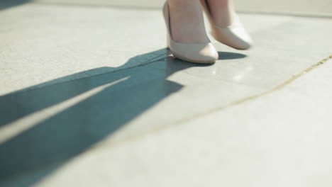 lower angle view of woman in heels walking out of building onto textured mat with sunlight casting shadow as door closes behind her, focus on movement, footwear, and modern office environment