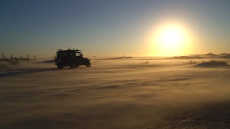 Silhouette-dune-buggy-explores-the-abandoned-terrain-of-the-sweltering-desert-during-a-sunset-sandstorm