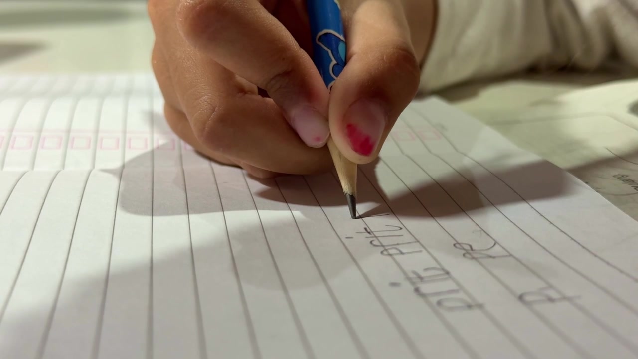 Dita di bambino che tengono una matita e scrivono lettere, pratica di scrittura a mano, concetto di educazione e apprendimento per bambini.