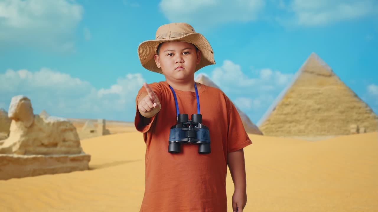 Asian Boy With A Hat And Binoculars Pointing His Finger Towards You And Shaking Head Waving Index Finger Avoid Offer While Traveling In Giza Pyramid. Boy Researcher Showing No Gesture