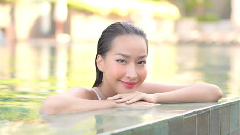 seductive asian woman in pool smiles and looks towards frame