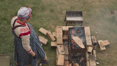 woman in traditional clothes watches over fire in brazier