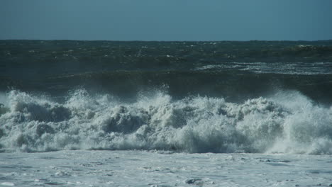 Large-waves-crashing-in-Half-Moon-Bay,-California-with-a-pod-of-dolphins-swimming-by-in-the-background