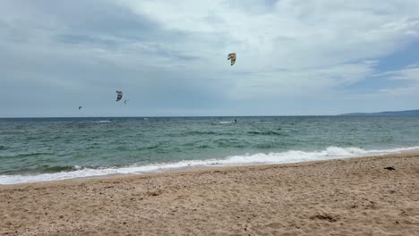 Gente-Practicando-Kitesurf-En-Una-Hermosa-Playa-Con-Cielos-Azules-Claros