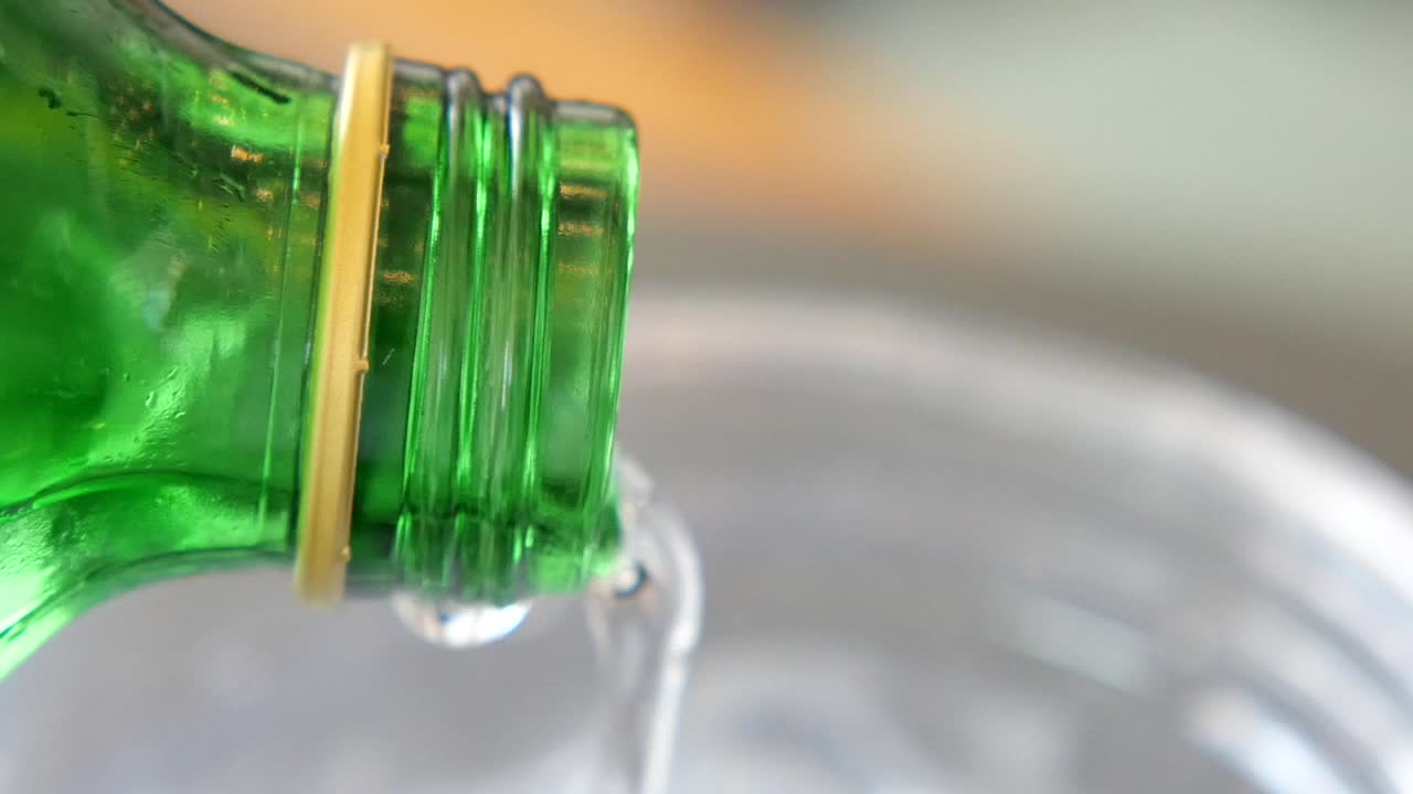 Pouring a clear liquid from a green bottle