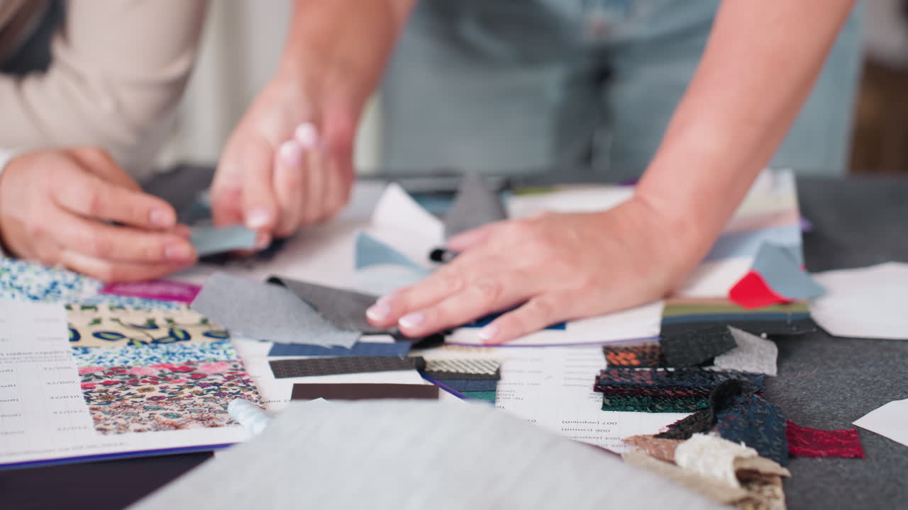 Fashion designers carefully checking textures and qualities of different colorful fabrics spread across table during material selection session, emphasizing creativity and attention to textile detail
