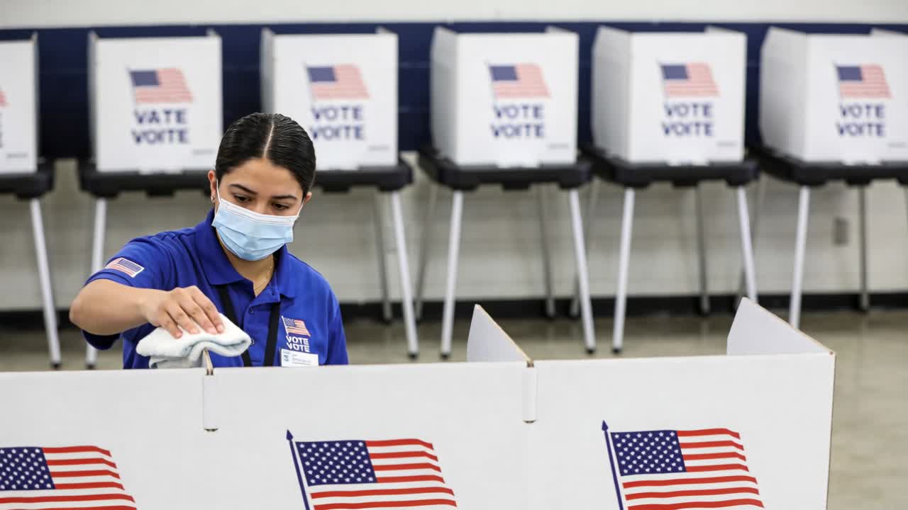 Wiping poll worker blue-polo mask cleaning voting partition at poll site with cloth before voting