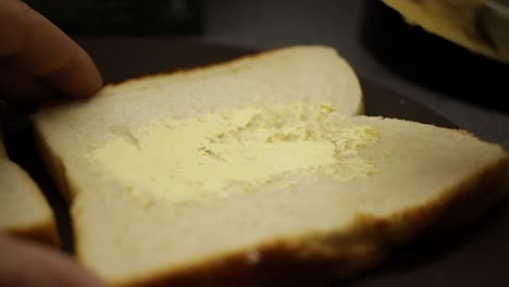 close up of a man's hand spreading butter onto a piece of white bread