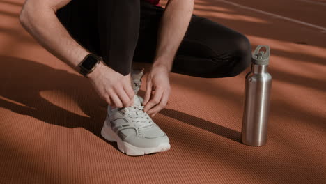 person tying shoelaces on a running track with water bottle