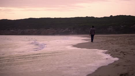 slowmotion shot of a man walking alongside the ocean during sunset