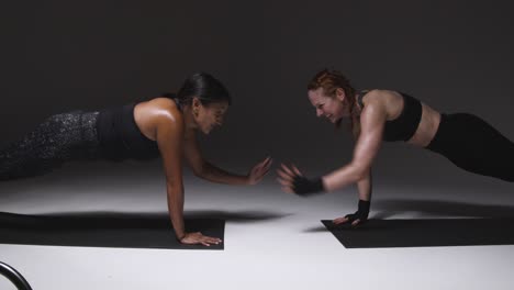 studio shot of two mature women wearing gym fitness clothing doing plank exercise together 1