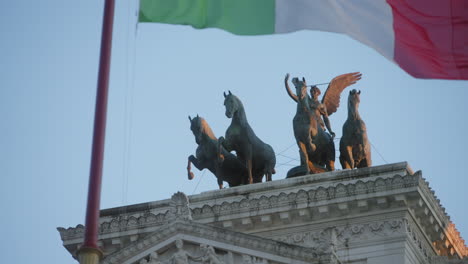 scultpure on top of vittorio emmanuel ii monument in rome, italy, with italian wave flying on the foreground
