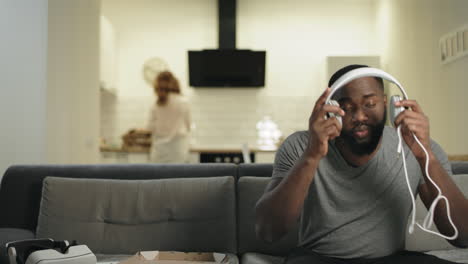 black man putting headphones at open kitchen. smiling guy making dance movement