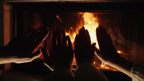 hands of a man and a woman bask in front of a fire in a fireplace