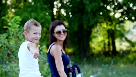 a woman and a boy are walking around the field, son is riding a pony, mother is holding a pony for a bridle. cheerful, happy family vacation. outdoors, in summer, near the forest