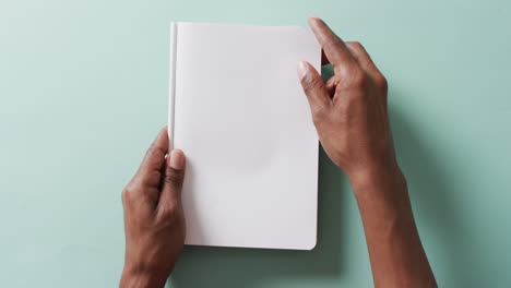 Close-up-of-hand-touching-a-book-with-copy-space-on-green-background-in-slow-motion