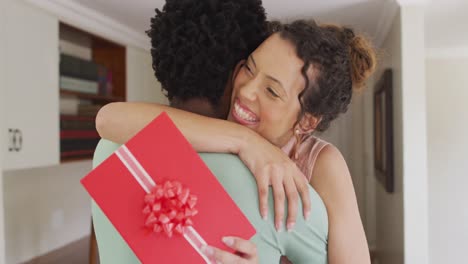 happy biracial woman hugging her partner and holding box with present