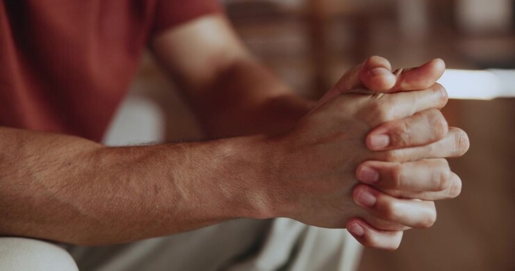 Primo piano di un uomo seduto con le mani giunte