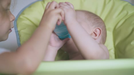 Schwester-Hilft-Dem-Jüngeren-Bruder,-Im-Hochstuhl-Wasser-Zu-Trinken