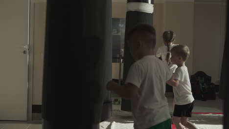 children group trains with punching bags in martial arts class. little fighters exercises kicking heavy inventory in sports school slow motion