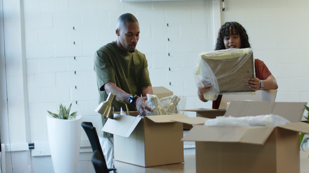 African American team unpacking new boxes, placing brass lamps and unwrapping frame at office area