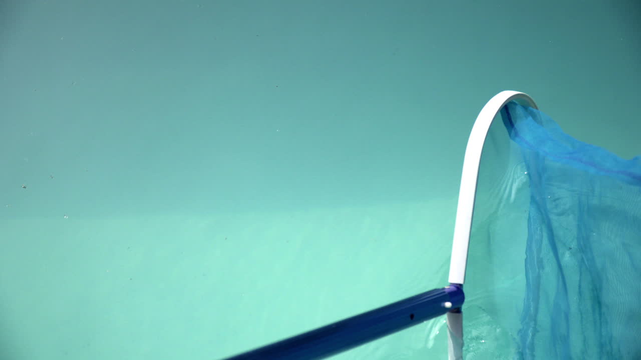 Closeup of a telescopic pool cleaning net scooping dirt off the surface of a swimming pool