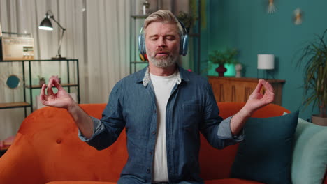 middle-aged senior man at home couch eyes closed meditating with concentrated thoughts, listen music