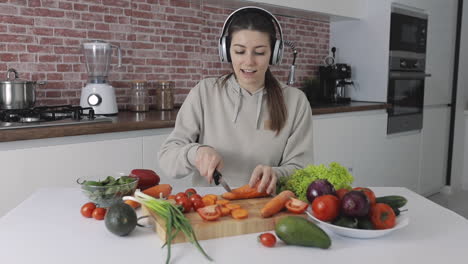 junge frau, die ein veganes rezept zubereitet, gemüse schneidet und musik hört