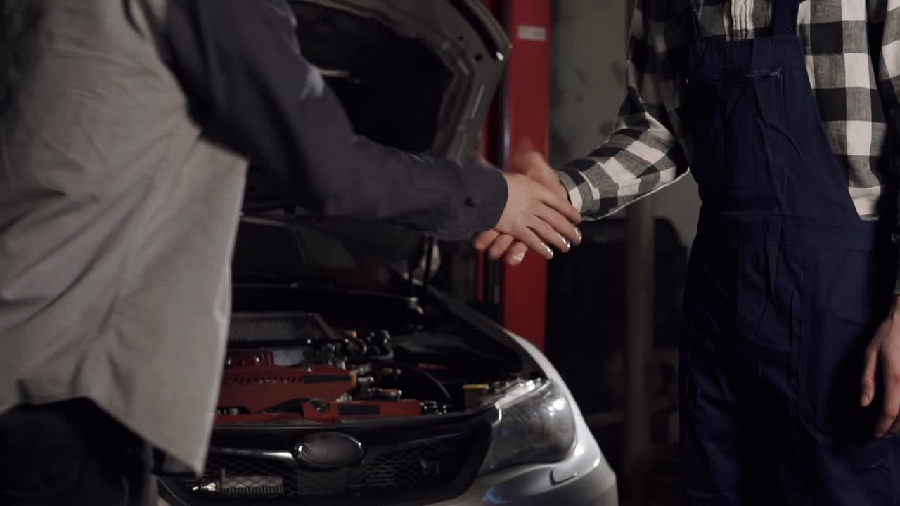 una foto de cerca del mecánico y el cliente estrechando la mano en un taller de reparación de automóviles.