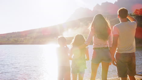 Parents-and-two-kids-standing-on-jetty-by-lake,-back-view