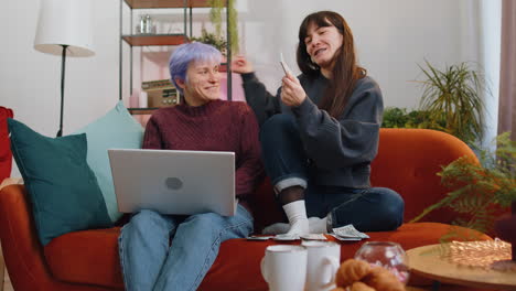 Lesbian-women-family-couple-counting-money-cash-use-laptop-computer-calculate-domestic-bills-at-home