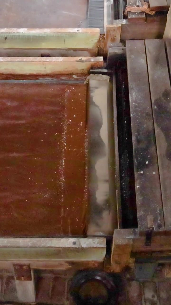 Wooden planks move through a traditional sawmill, showcasing the mechanical process in a historic setting with natural lighting