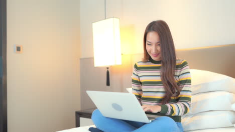 happy woman exults while working on computer laptop sitting on bed