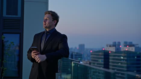 a cheerful businessman celebrates after receiving good news on his smartphone, with a sunset skyline behind him, symbolizing success and achievement