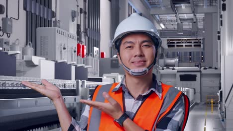 close up of asian male engineer with safety helmet smiling and pointing to side while standing at pharmaceutical factory, vaccine production facility