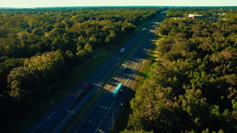 great motorway surrounded by plenty high trees semi trucks and personal cars traveling across long roads opposite directions vivid saturated colours horizon between earth and sky cinematic drone view