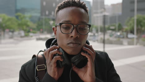 retrato en primer plano de un hombre afroamericano de moda estudiante pasante con auriculares escuchando música usando un teléfono inteligente en una ciudad urbana
