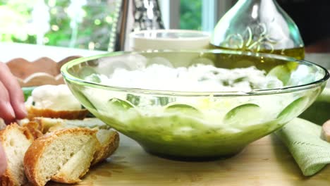 placing bread on a wood cutting board. making tzatziki greek or mediterranean sauce or dip for a party. dip or sauce in a green bowl on a wooden cutting board with dill, green napkin and a grater.