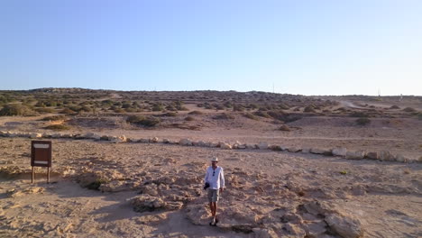 Aerial-shot-of-a-photographer-approaching-the-edge-of-the-cliff-and-taking-pictures-of-the-beautiful-sea-caves-below-him