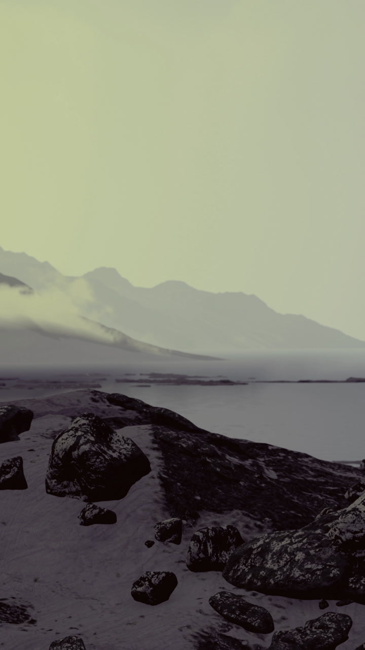 Mountains and fog over the calm sea with rocks on the shore at sunset