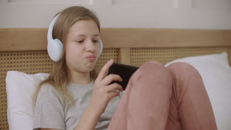 teen girl is playing internet games in cellphone at home lying in bedroom in sunday morning and communicating online