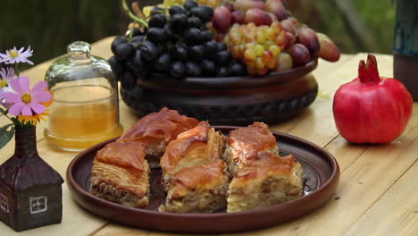 Teller-Voll-Mit-Frisch-Zubereitetem-Baklava-Auf-Dem-Tisch-Neben-Obstschale-Und-Rotem-Granatapfel