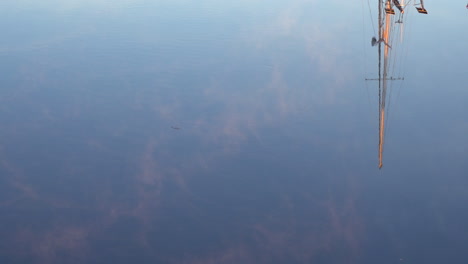 a mast reflects in the water at a harbor in this artistic shot