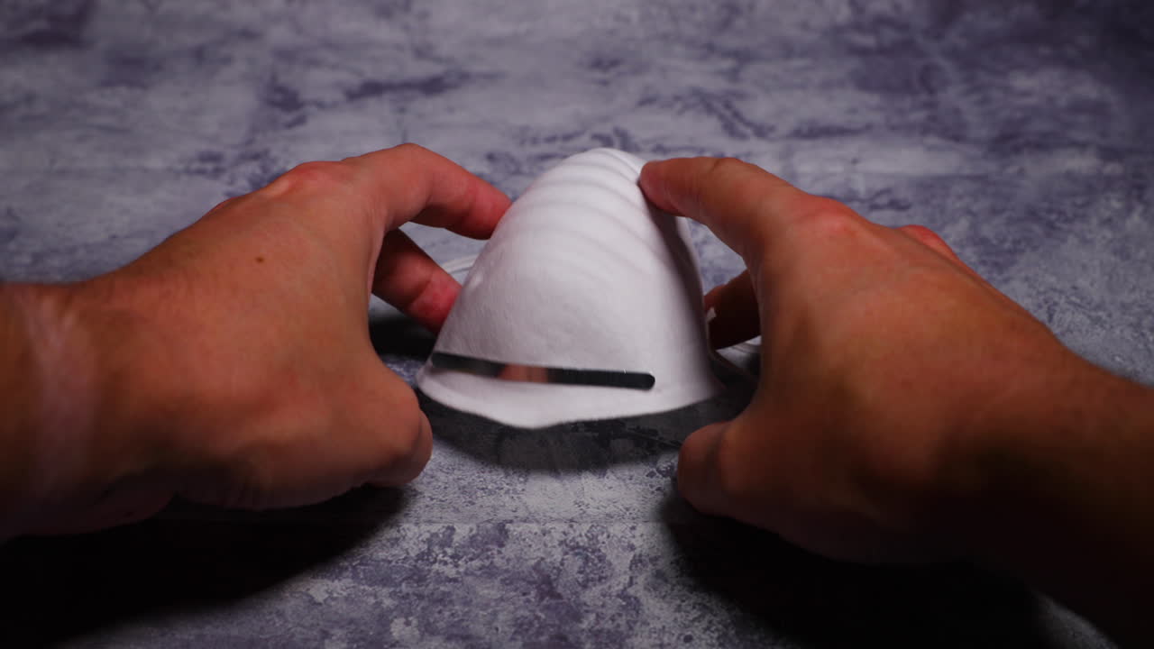 Men's hands first person view taking and putting protective face mask on camera white mask from threat like corona Covid-19 virus protects mouth and nose from dark black board capture in 4k 60fps